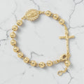 Pulsera rosario dorada de esfera gruesa con medalla y crucifijo sobre mármol blanco