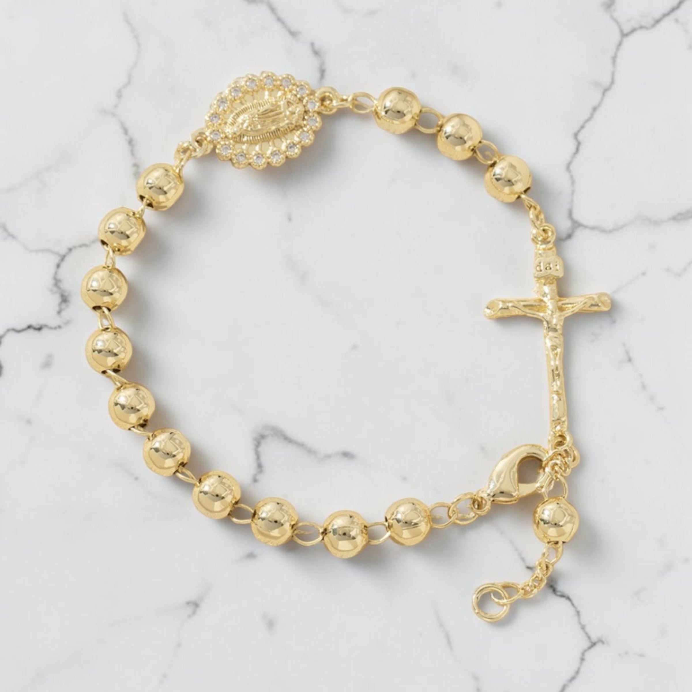 Pulsera rosario dorada de esfera gruesa con medalla y crucifijo sobre mármol blanco